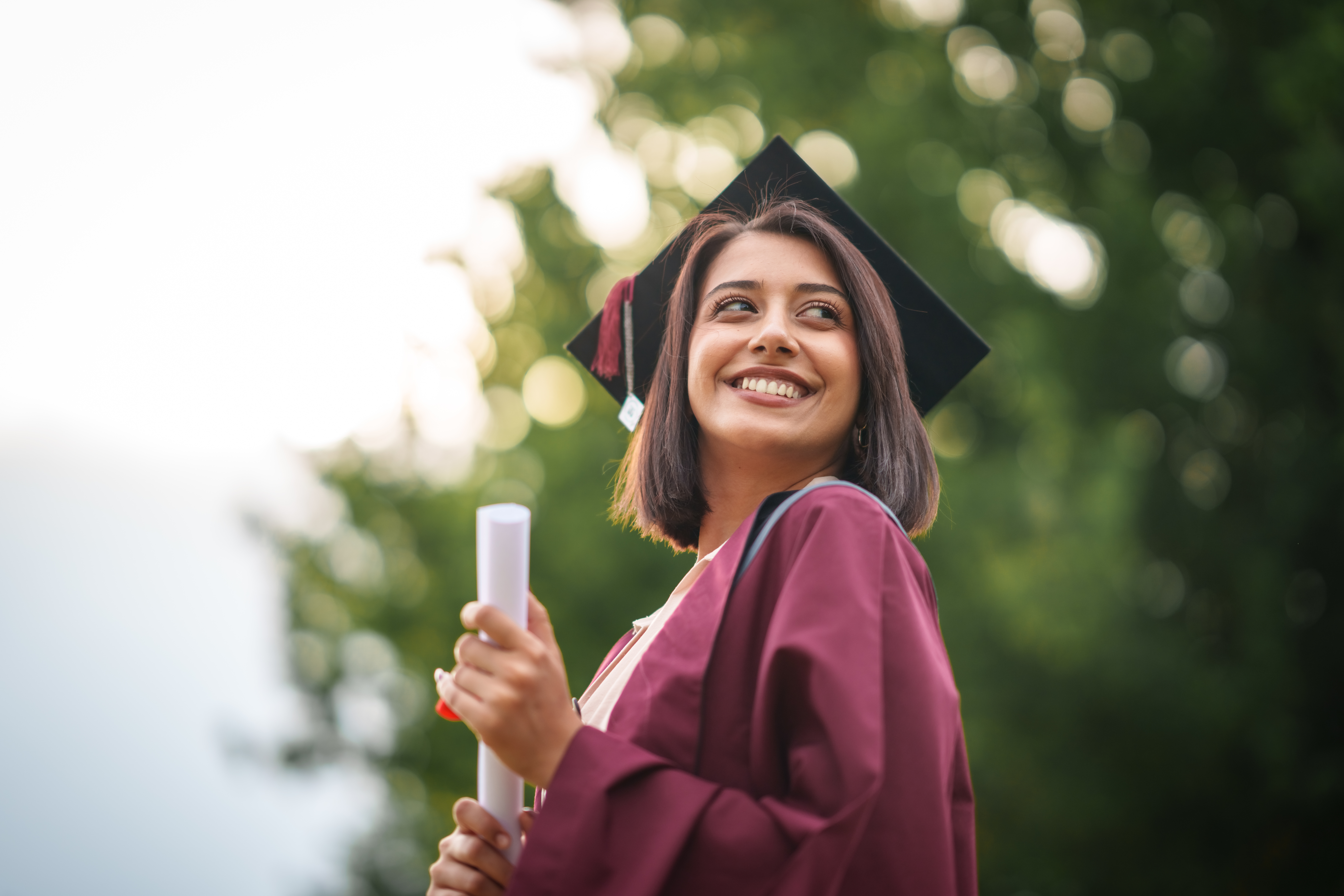 Smiling graduate in a cap and gown holding diploma 